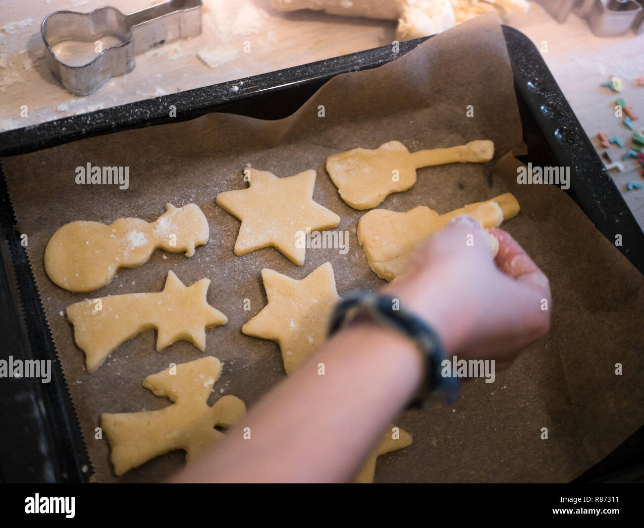 Christmas Bakery: Little girl putting different shapes of cookie dough on a baking tray - snowman, star, guitar, angel Stock Photo