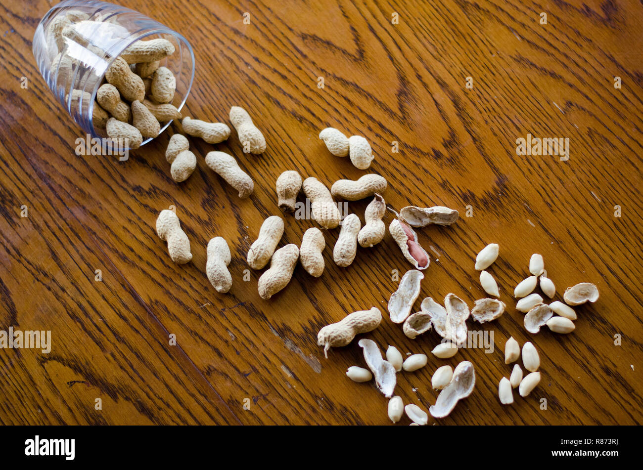 Peanuts from a glass fallen all over the wooden table. Stock Photo