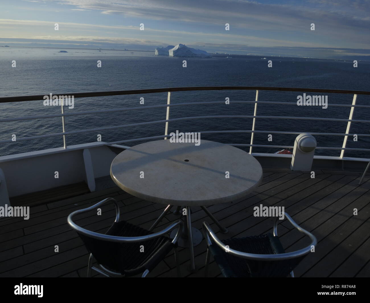 Ilulissat Eisberge am Abend Zwei leere Stühle vor einem leeren Tisch auf dem Deck eines Kreuzfahrtschiffes mit Blick auf die eisige Kulisse, Stock Photo