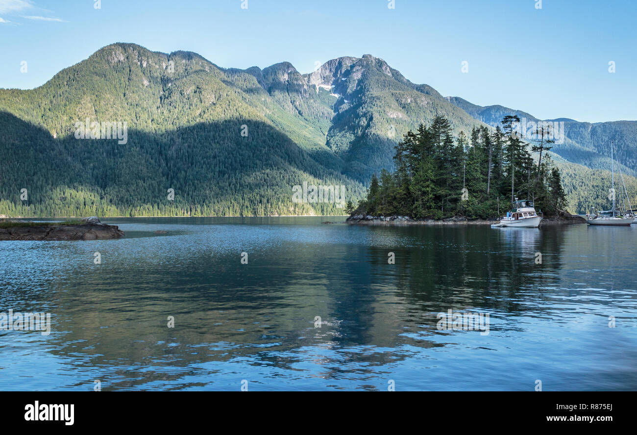 Boats anchored in a BC inlet are in evening shade while mountains on the far shore are still in sunlight, save for a shadow from a passing cloud. Stock Photo