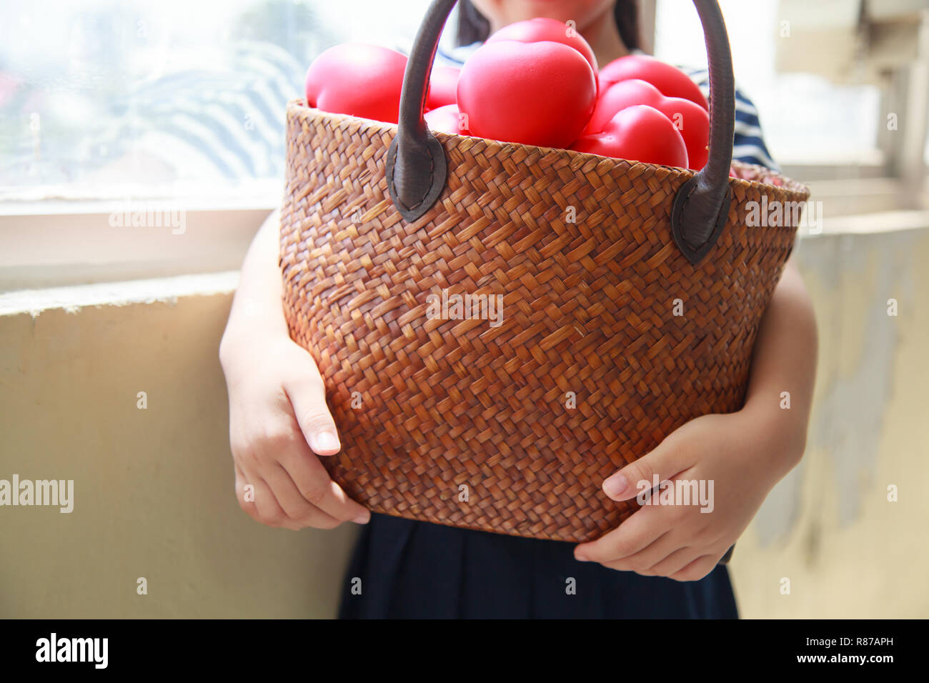 girl in navy blue striped dress handing basket of red hearts represents helping hands, family support, morale, purity, innocence, cheer up, loves, hos Stock Photo