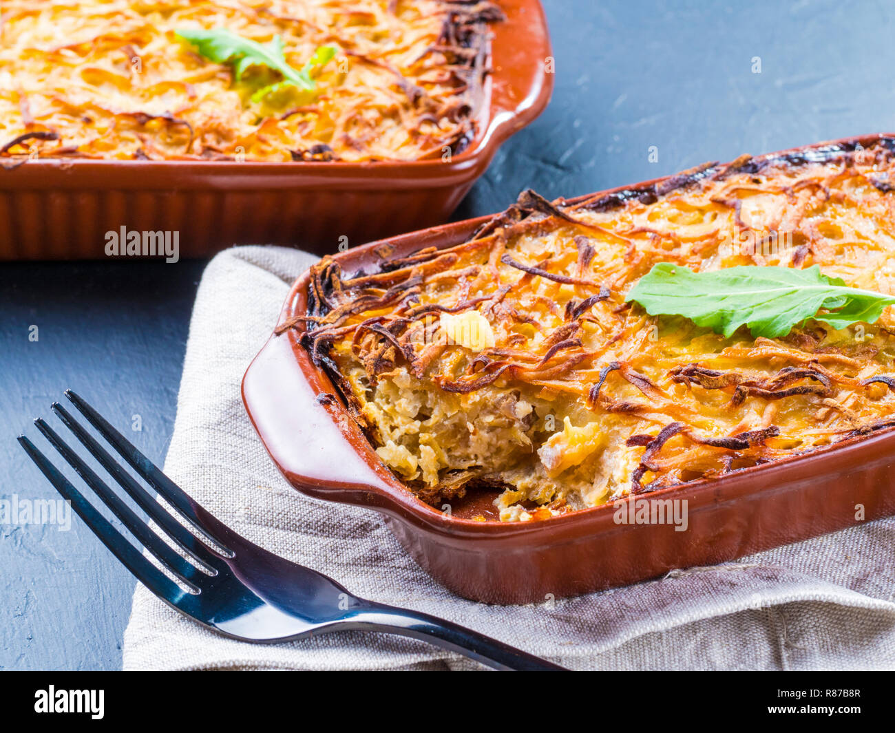Close up view of appetizing potato casserole with fish, eggs and cream. Potato casserole in serving baking dish on dark concrete background Stock Photo