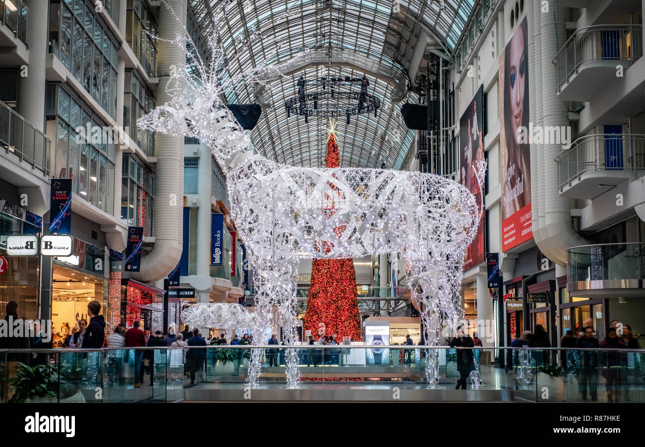Toronto, Ontario, Canada - Dec 12, 2018: Busy Christmas shoppers walk by a huge white reindeer, illuminated with white lights, inside the Eaton Centre Stock Photo