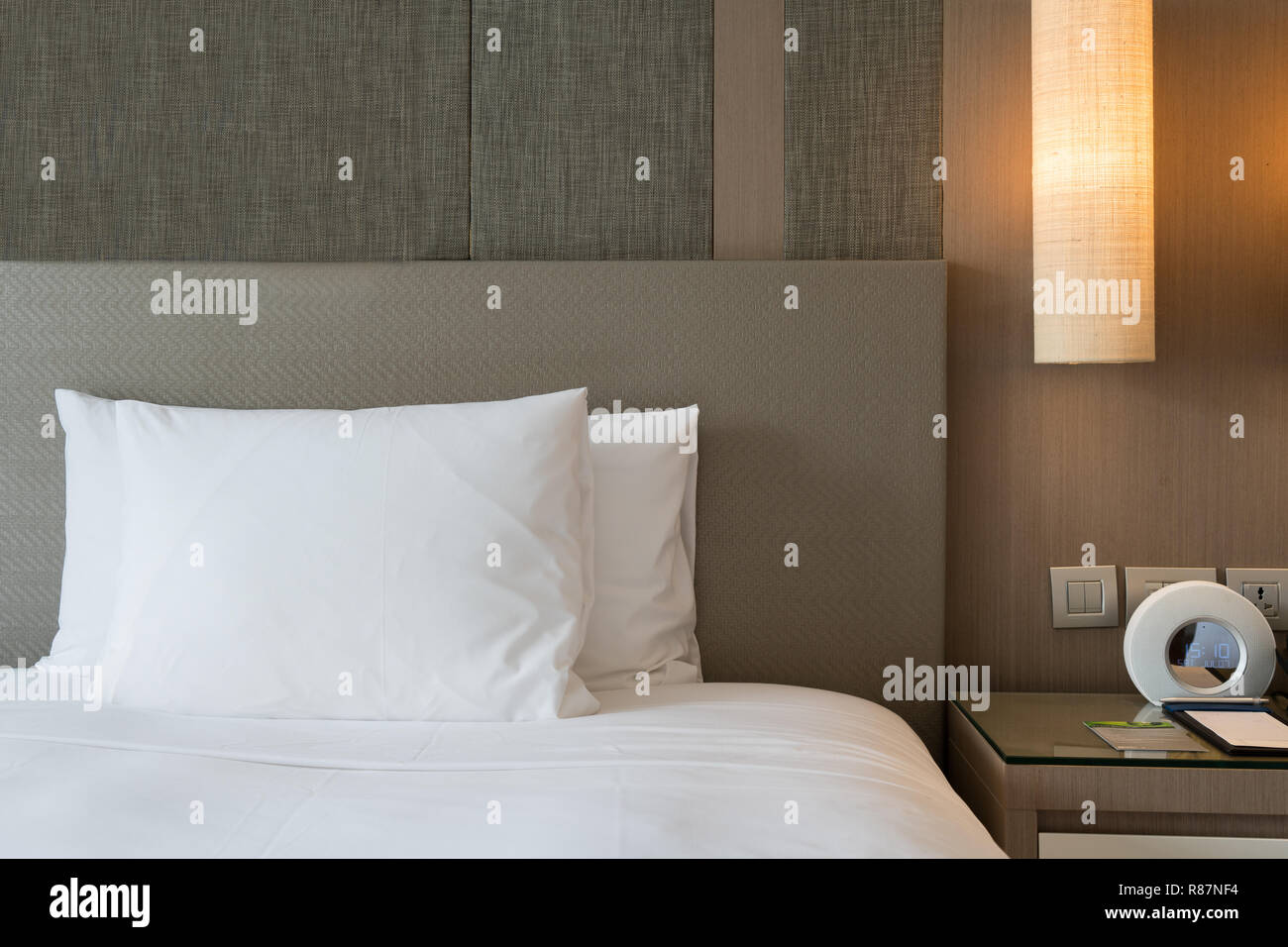 Close up fragment of bedroom with reading lamp and digital alarm clock in modern home or hotel. Stock Photo