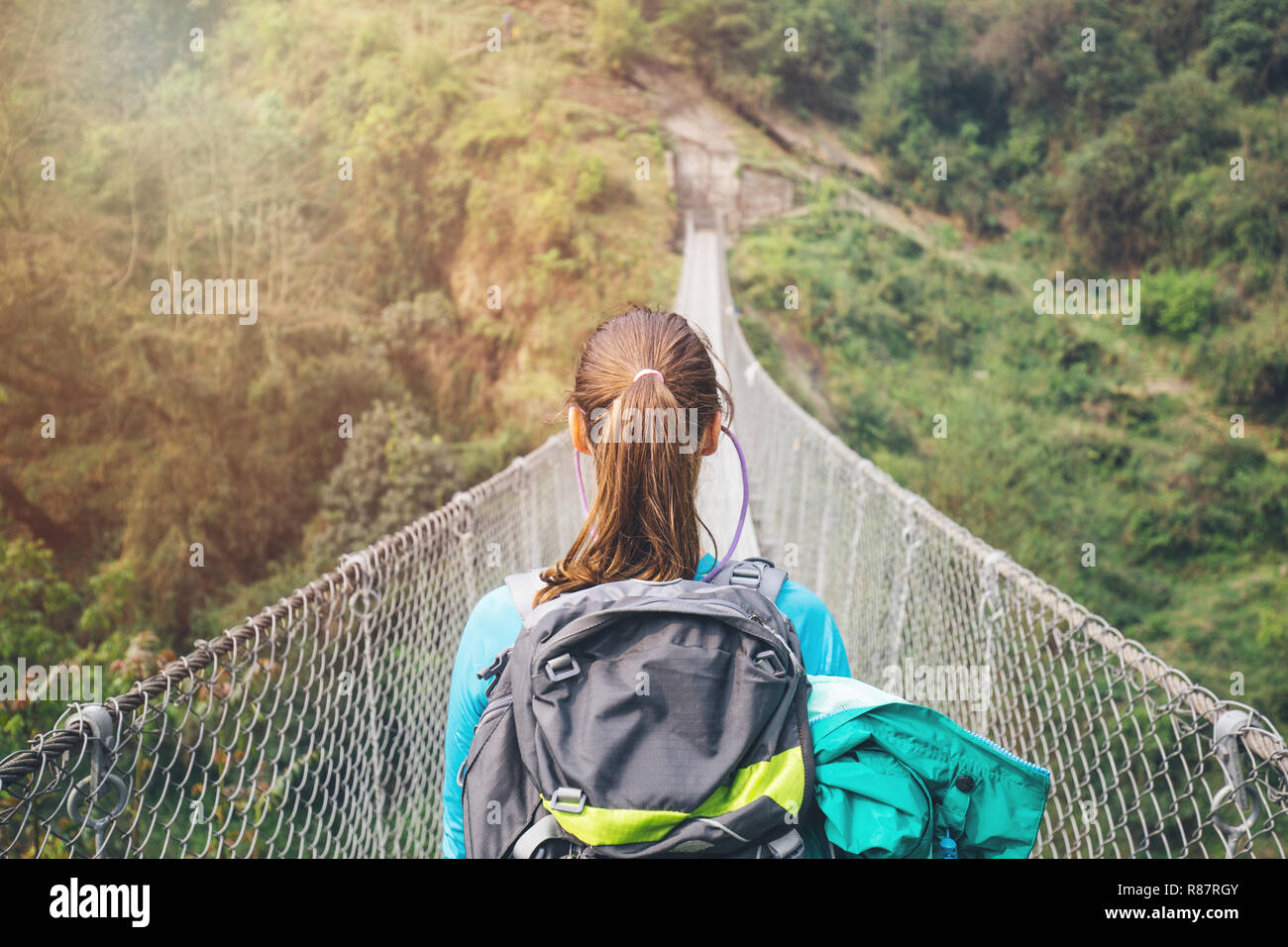 Rear view of girl with backpack crossing the suspension bridge Stock
