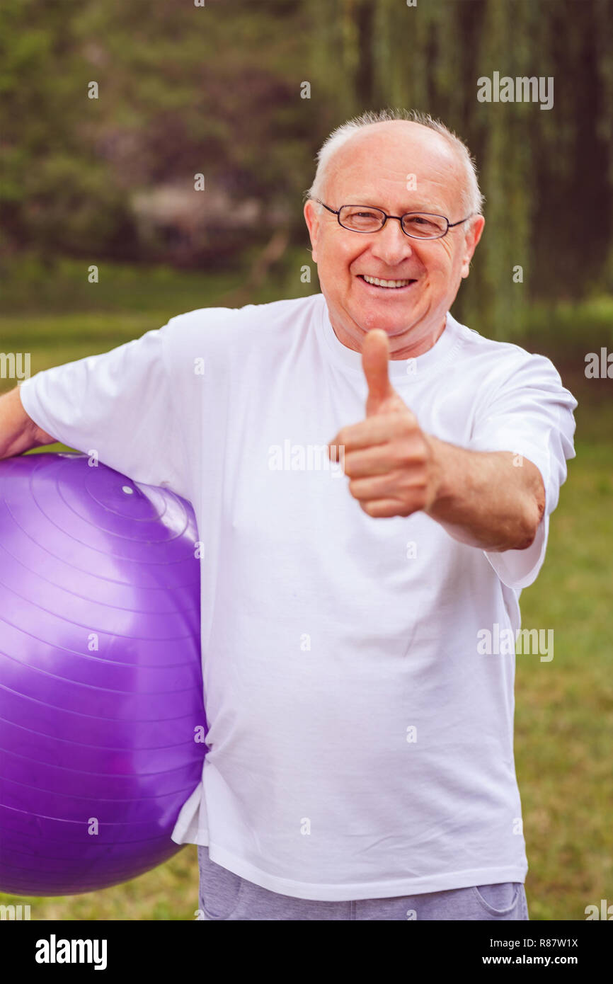 thumb up for healthy exercising – Smiling senior man with fitness balls in park and exercising Stock Photo