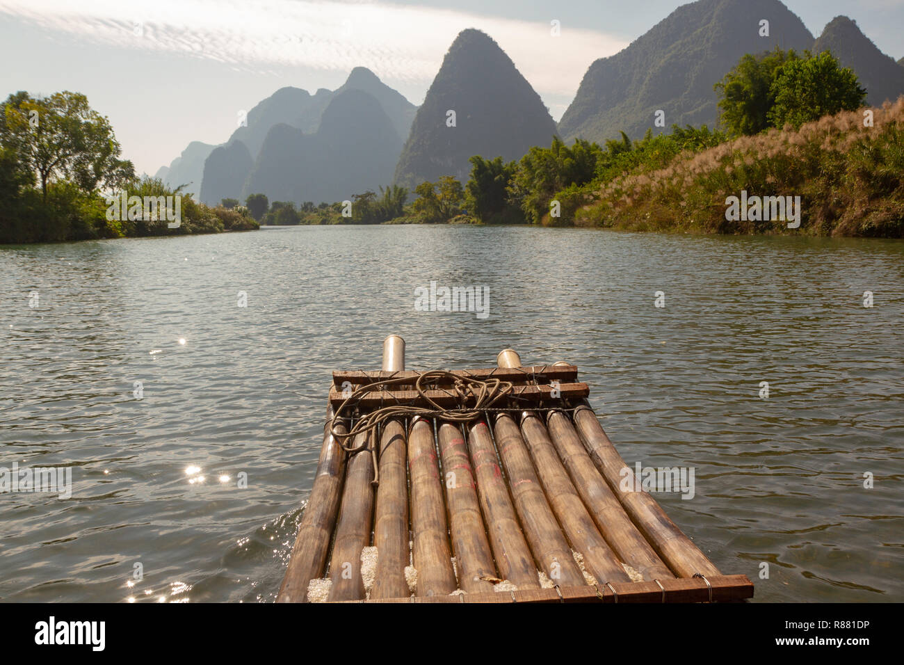 Front of bamboo raft in foreground on Yulong River, Yangshuo, China. Limestone cliffs in silhouette along edge of river. Stock Photo