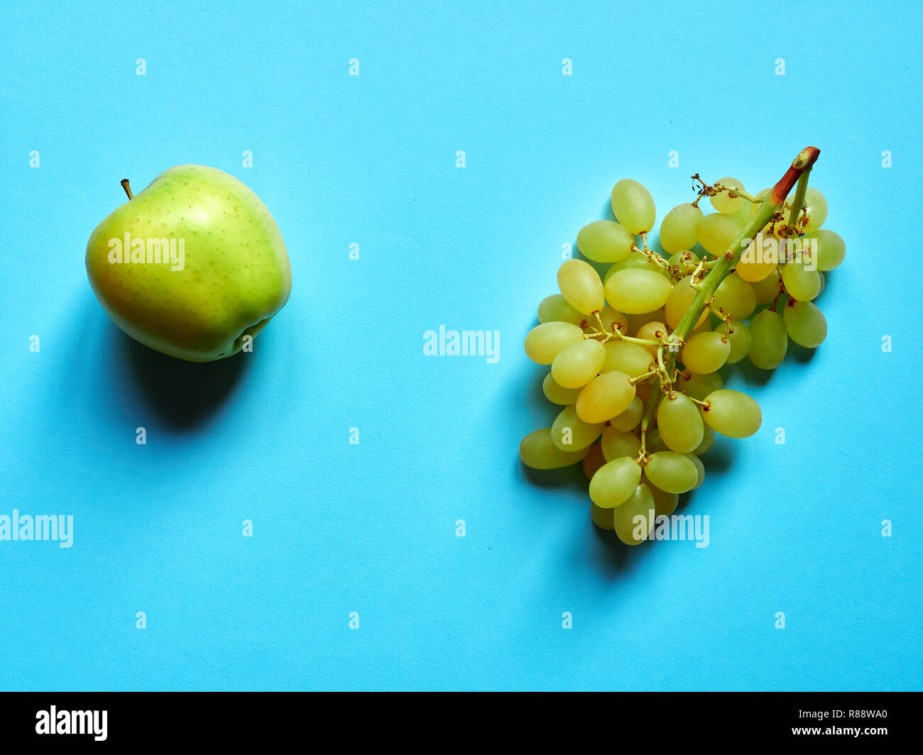 Green apple and bunch of green grapes isolated in studio against a blue background viewed from above Stock Photo