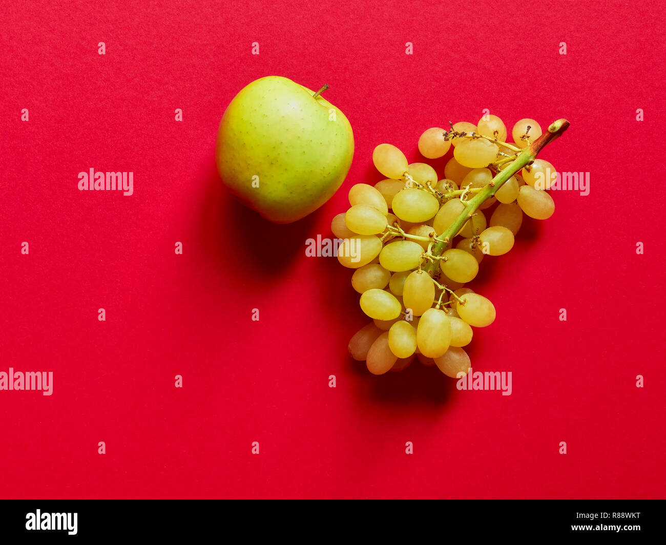 Green apple and bunch of green grapes isolated in studio against a red background viewed from above Stock Photo