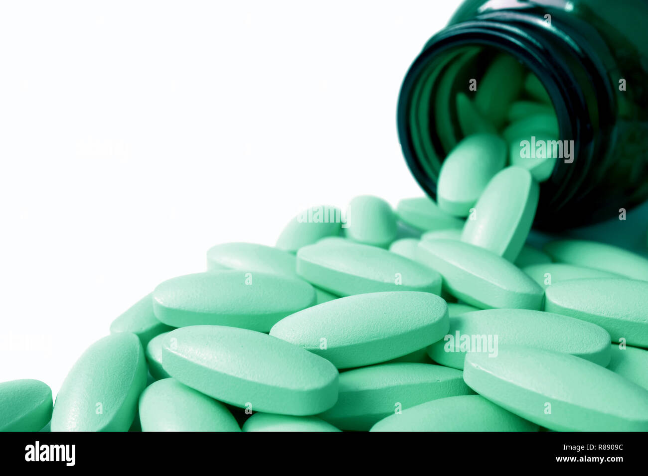 Heap of light mint green color oval shaped pills scattered from glass