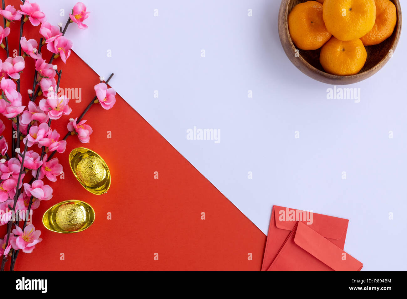 Flat Lay Chinese New Year Background - Cherry Blossom, Mandarin Orange, Red Envelop and Golden Ingots on dual tone background red and white. Stock Photo