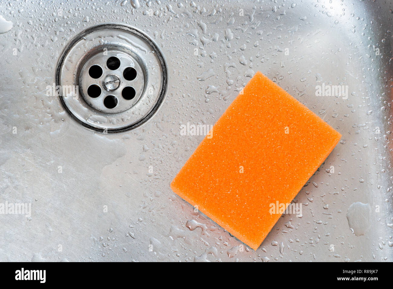 orange sponge and drain of stainless kitchen sink closeup Stock Photo