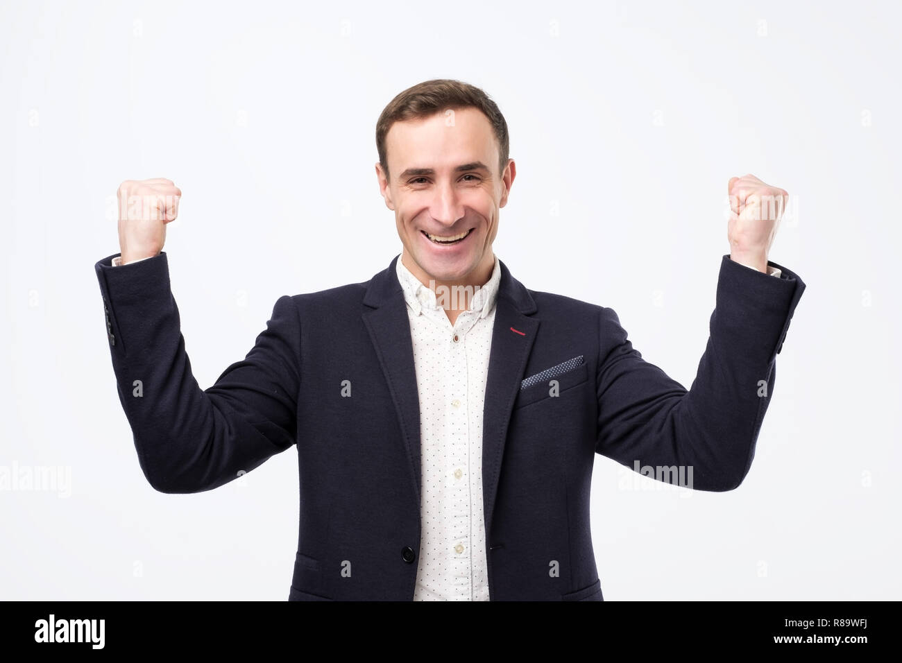 Pleased and happy young italian man is smiling broadly and showing victory sign with both hands. Stock Photo