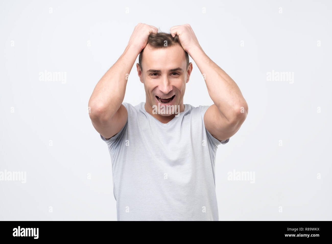 Young man who can not believe in his own happiness, being excited, holding hands on hair Stock Photo