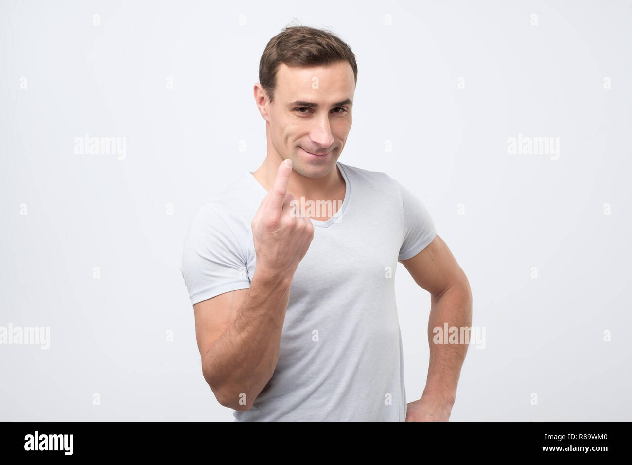 Handsome young man showing come here gesture with index finger and smiling over gray background