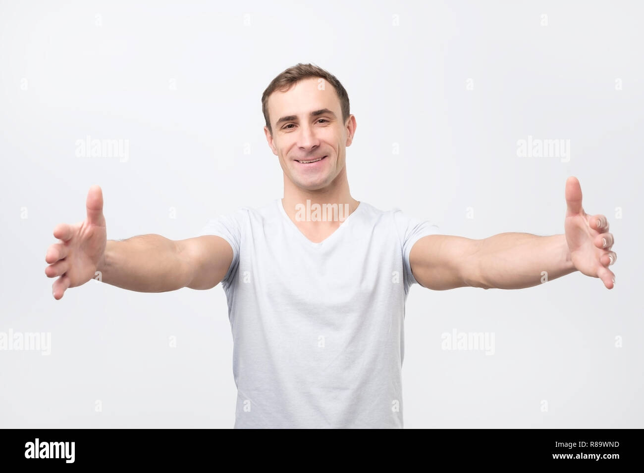 Handsome guy pulling hands towards camera and smiling friendly at camera wanting hug Stock Photo