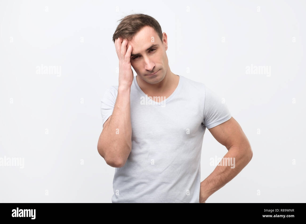 Serious italian male has attentive look, keeps hand on head, looking down. Stock Photo