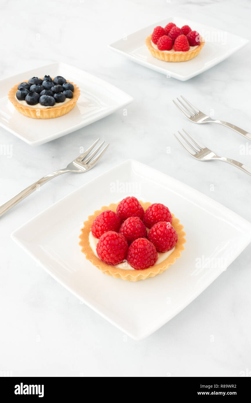 Homemade raspberry and blueberry tartlets filled with vanilla cream on