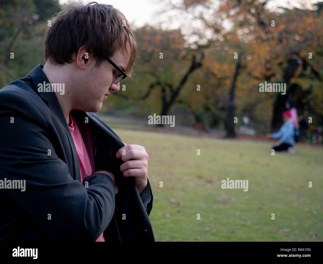 A man taking something out of his jacket pocket while sat on a park
