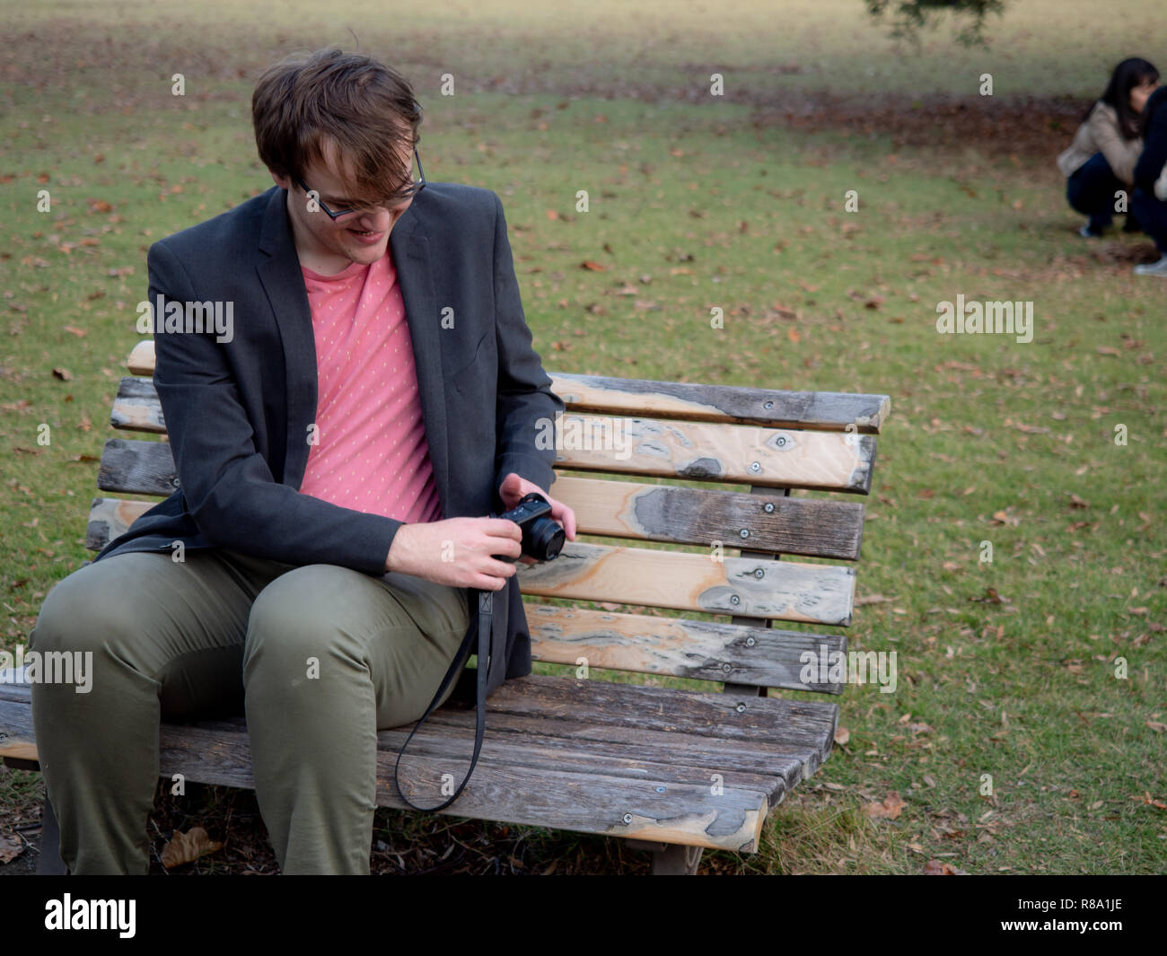A Man Sat On A Park Bench Taking Pictures With His Digital Camera