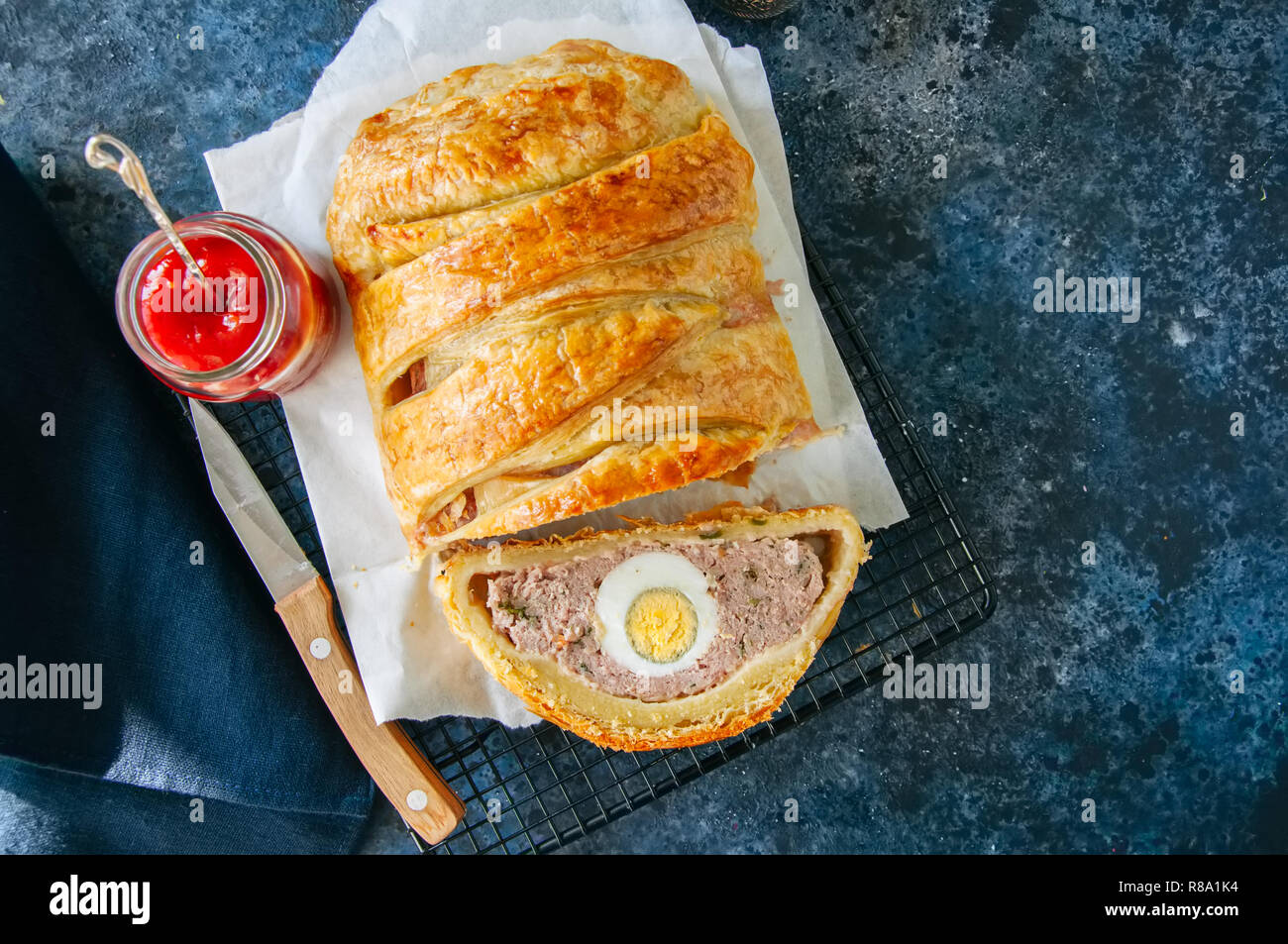 Turkey meatloaf with egg filling in a puff pastry served on a wire rack. Blue stone backdrop. Stock Photo
