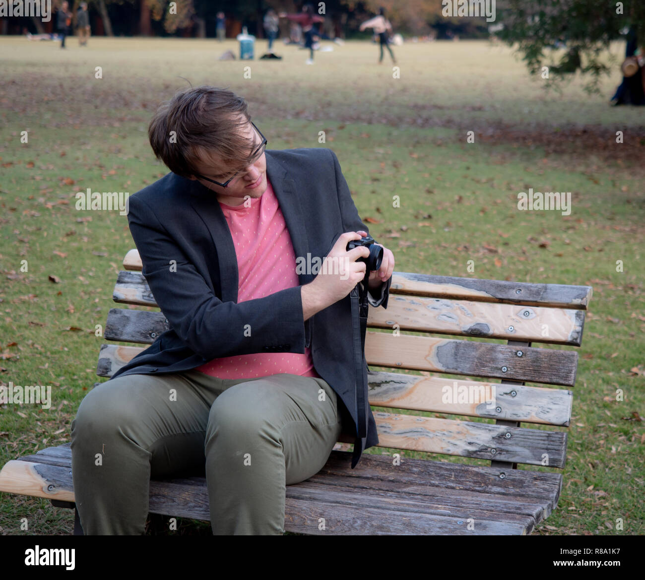 A Man Sat On A Park Bench Taking Pictures With His Digital Camera