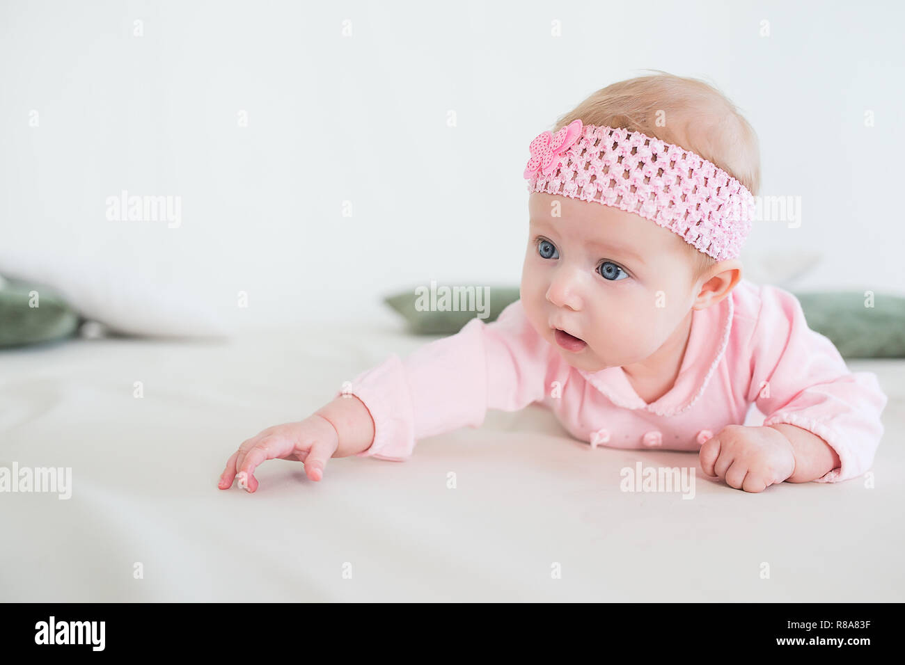 baby lying on his stomach on the floor and looking forward. Beautiful baby girl in pink. Stock Photo
