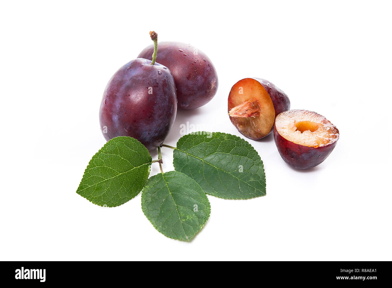 Two whole and half of sweet juicy plums with big green leaf isolated on ...