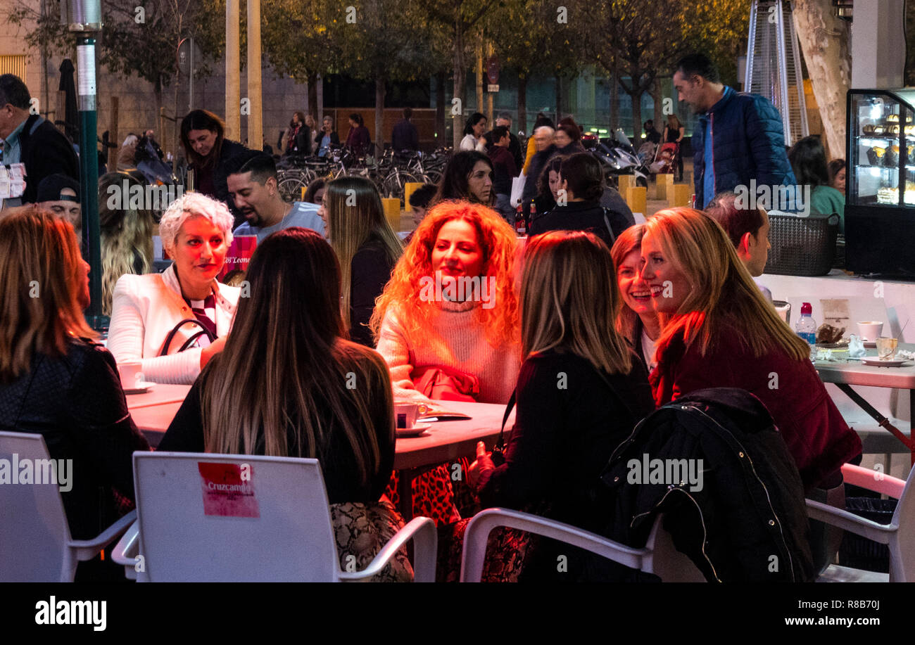 Female friends having a drink at a cafe bar in Seville, Spain.  The red light on blonde woman is from a space heater. Stock Photo