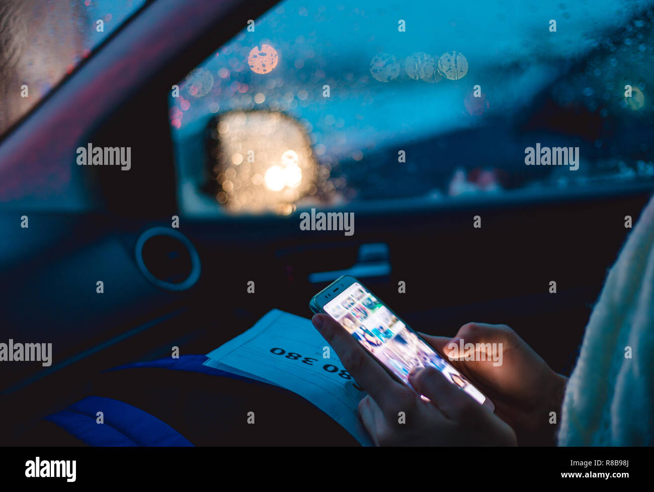 A woman sits in the passenger seat of a car and uses a smartphone in the early winter morning. Stock Photo