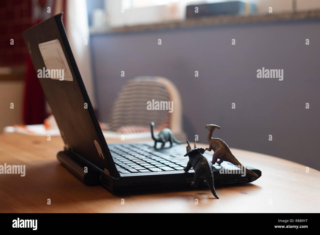 Open laptop on wooden table with small dinosaur toys that seem looking at the screen. Natural light. Smartworking during lockdown symbol. Stock Photo