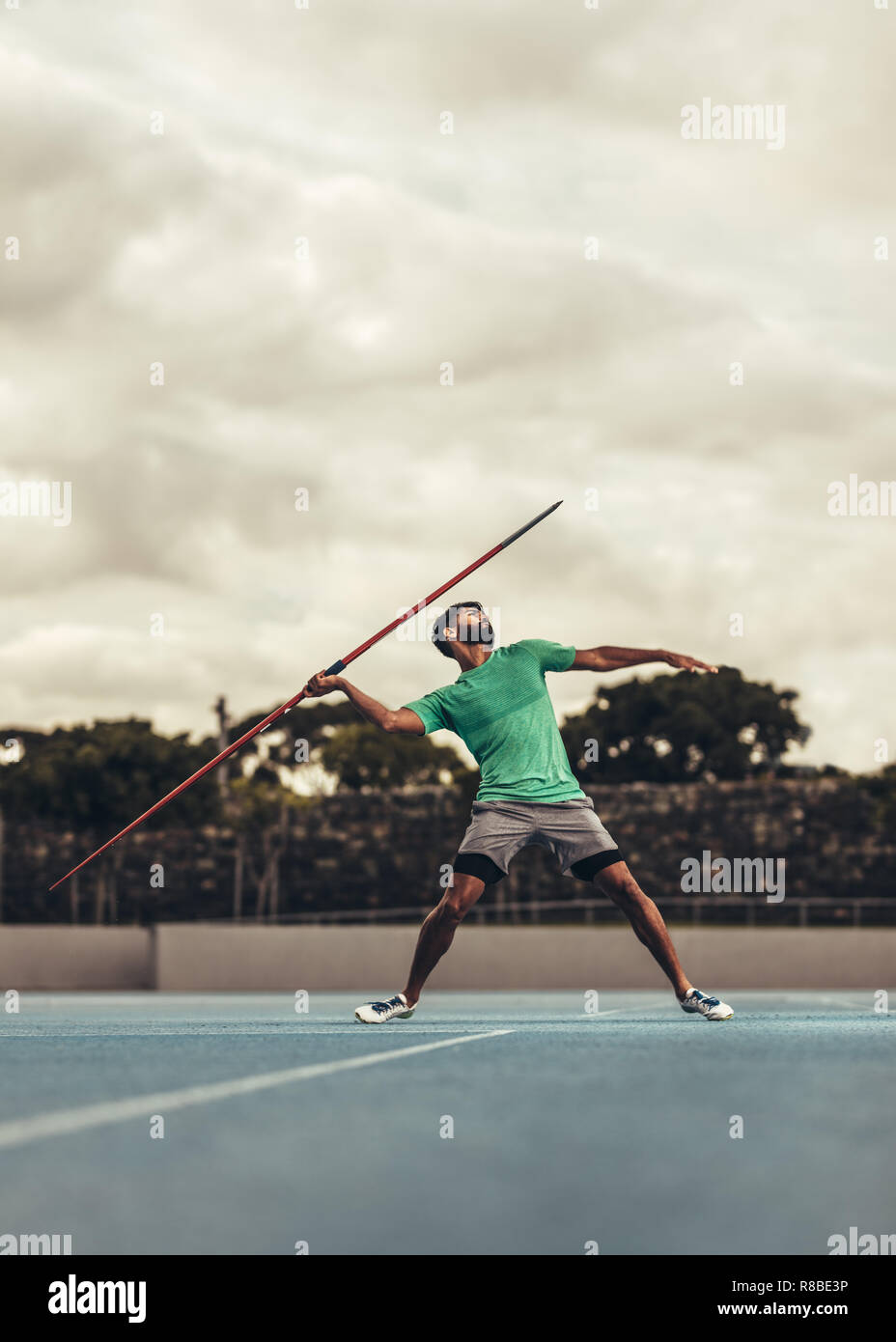 Man in position to throw a javelin in a track and field stadium. Athlete doing javelin training in the field on a cloudy day. Stock Photo
