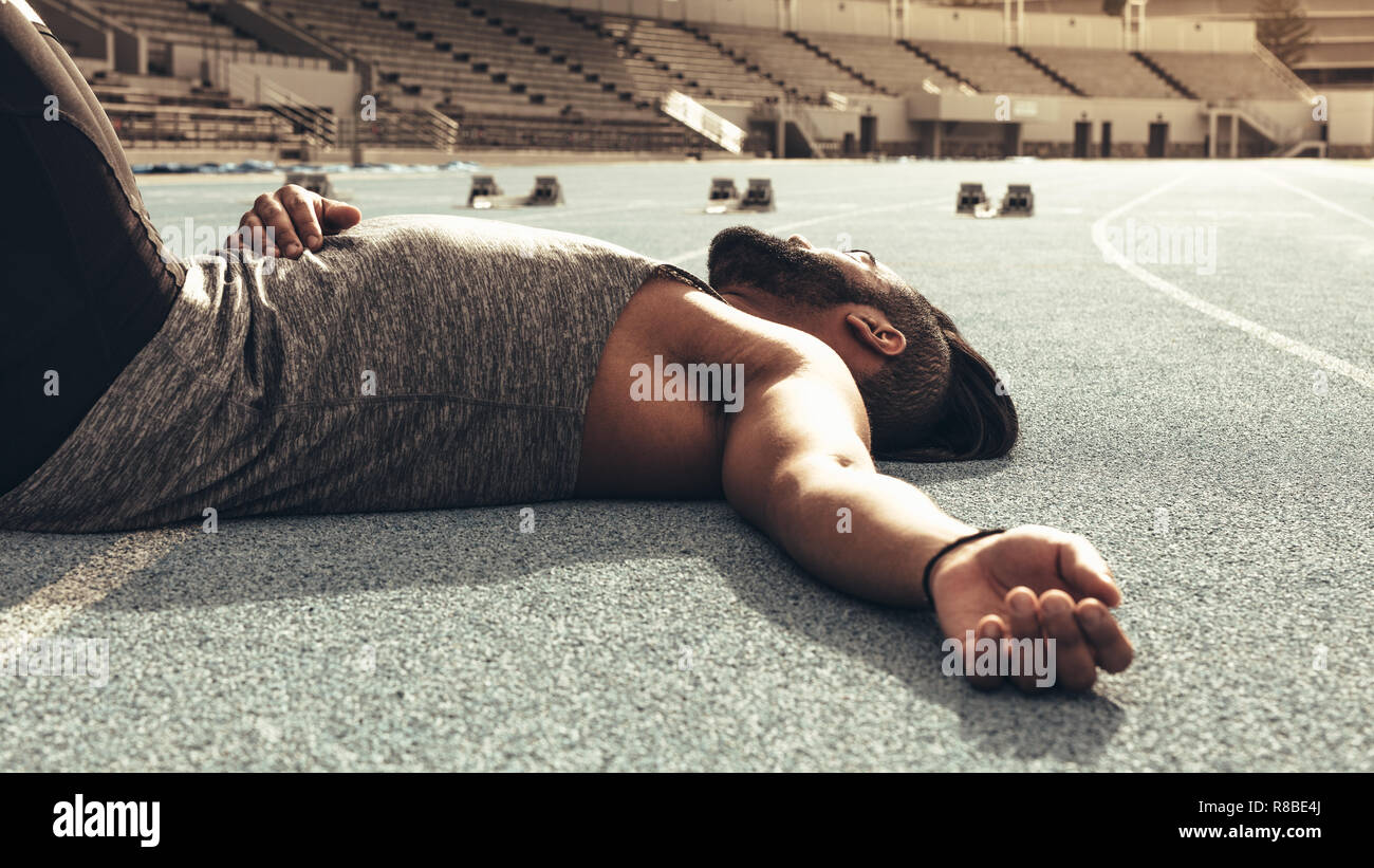 Runner lying on the track resting after a race. Close up of a tired athlete relaxing after a run. Stock Photo