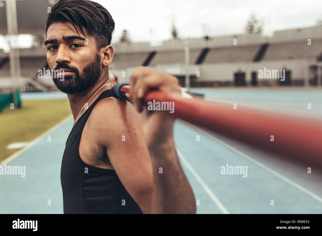 Close up of an athlete standing on track holding a javelin on his shoulders. Man training in javelin throw in a stadium. Stock Photo