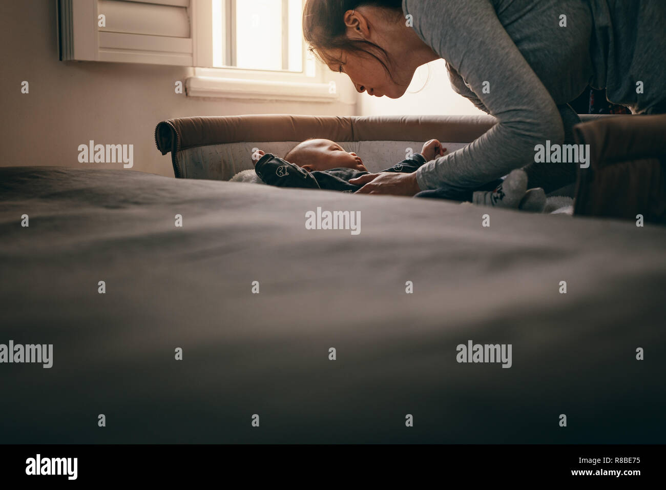 Mother putting her baby to sleep in his crib. Woman bending forward to lay the baby on the bed