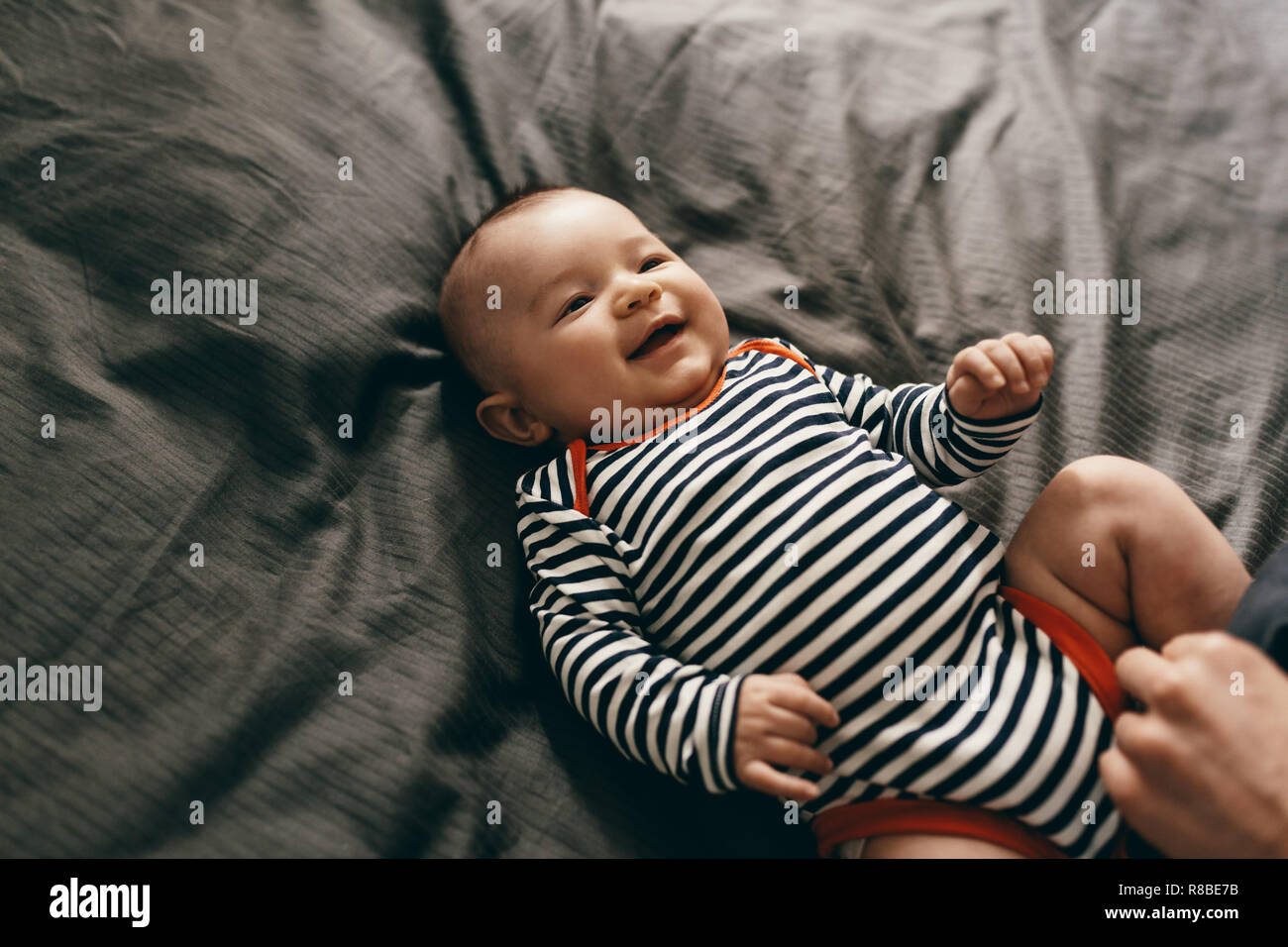 Top view of a smiling infant lying on bed. Cheerful little baby in a playful mood lying on bed. Stock Photo