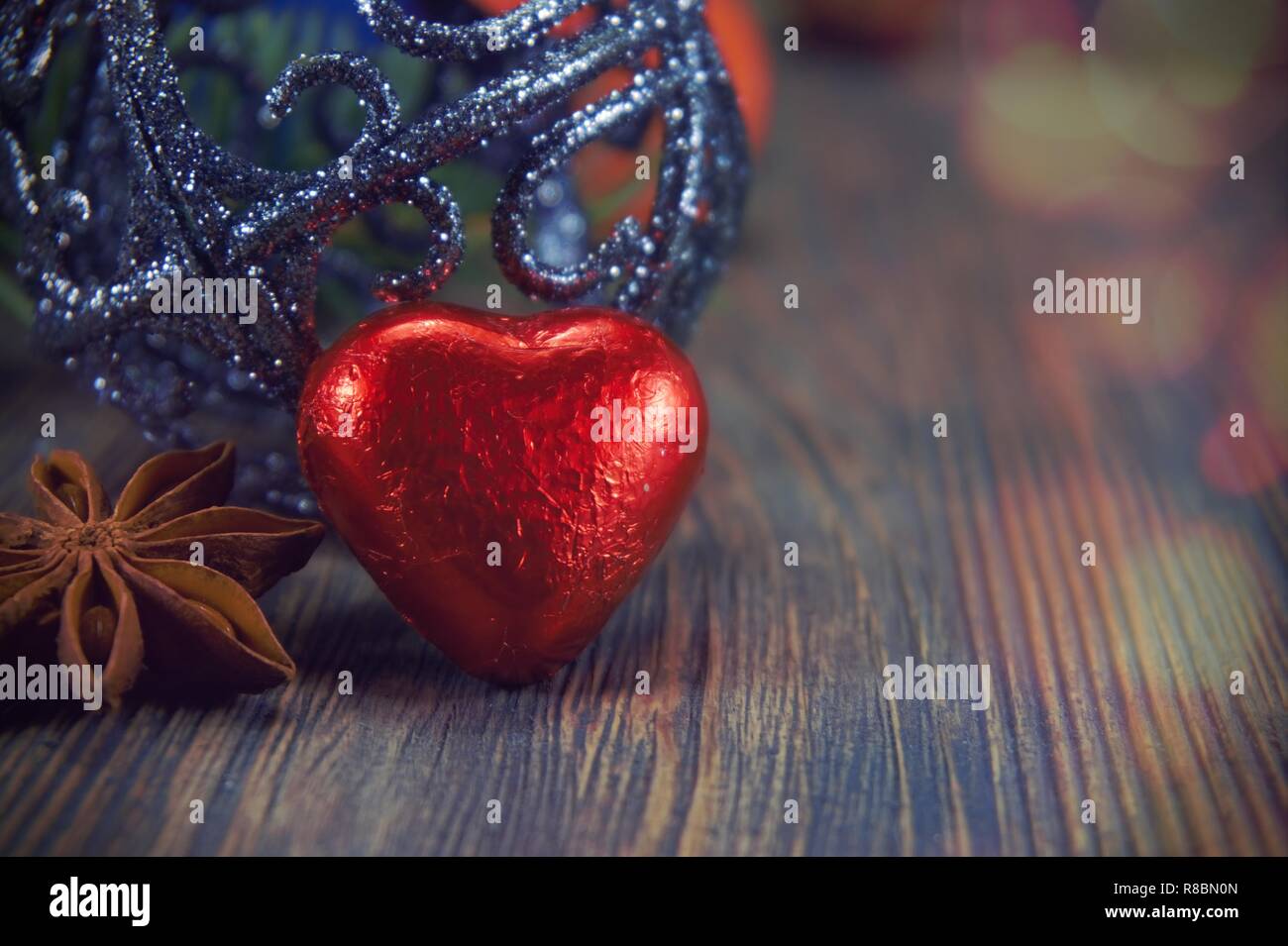 Red heart shaped chocolate and anise star next to christmas ball sitting on weathered wood surface background with copy space. Stock Photo