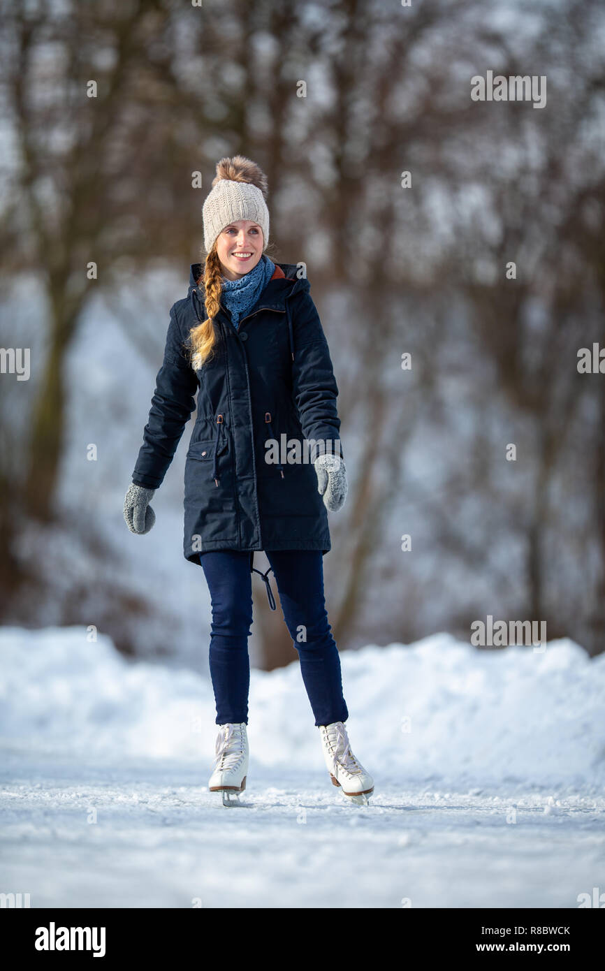 Young woman ice skating outdoors on a pond on a freezing winter day ...