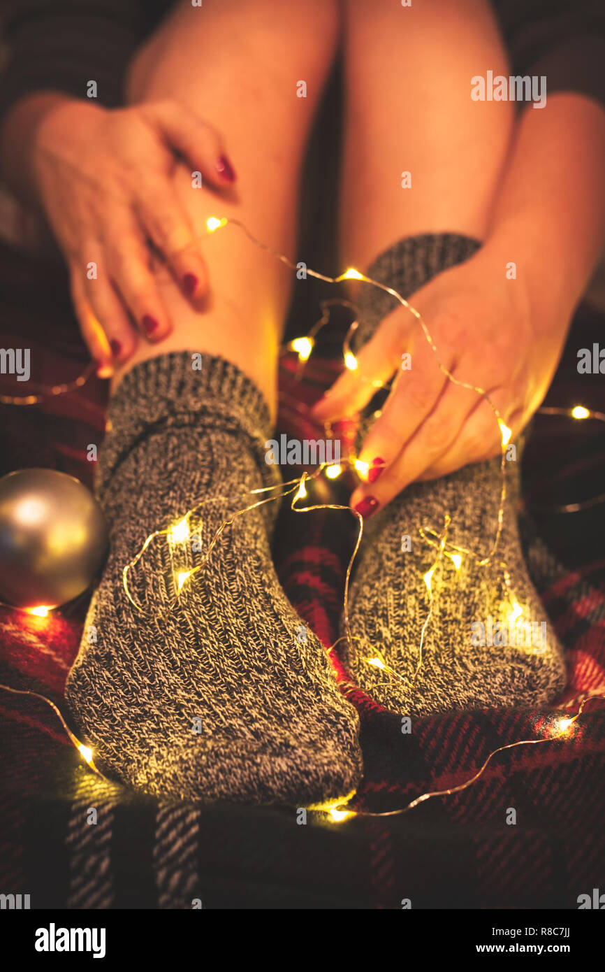 Woman's legs in cozy wool socks on a warm red blanket intertwined with fairy lights Stock Photo