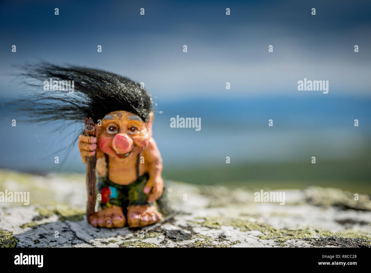 Happy troll out in the nature with his walking stick and black hair. Hair, hike, nature, wilderness, camping concept. Stock Photo