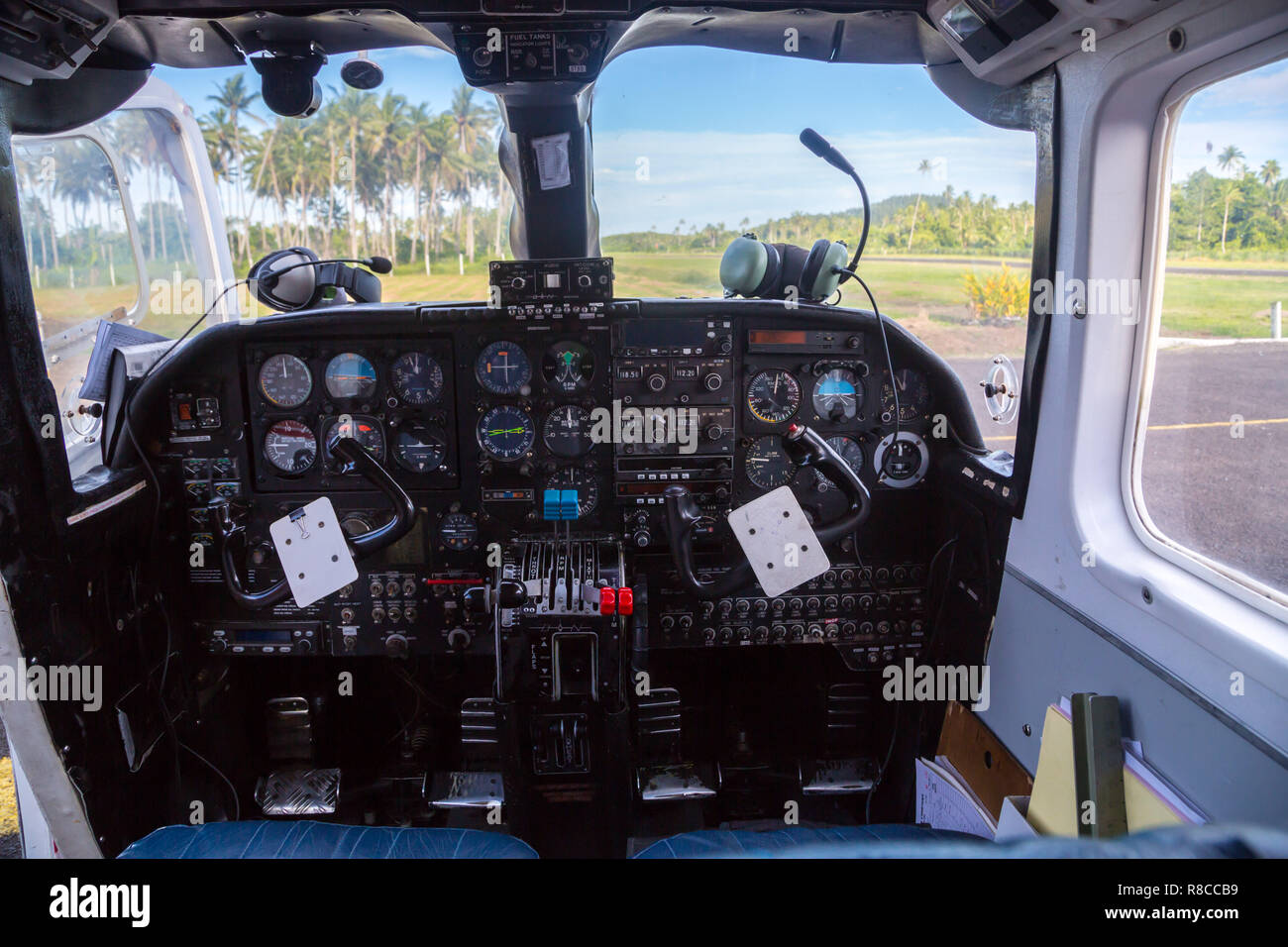 Air travel in Fiji, Melanesia, Oceania. View from a flight deck cockpit window of a small airplane to a lost remote airstrip overgrown with palms. Stock Photo