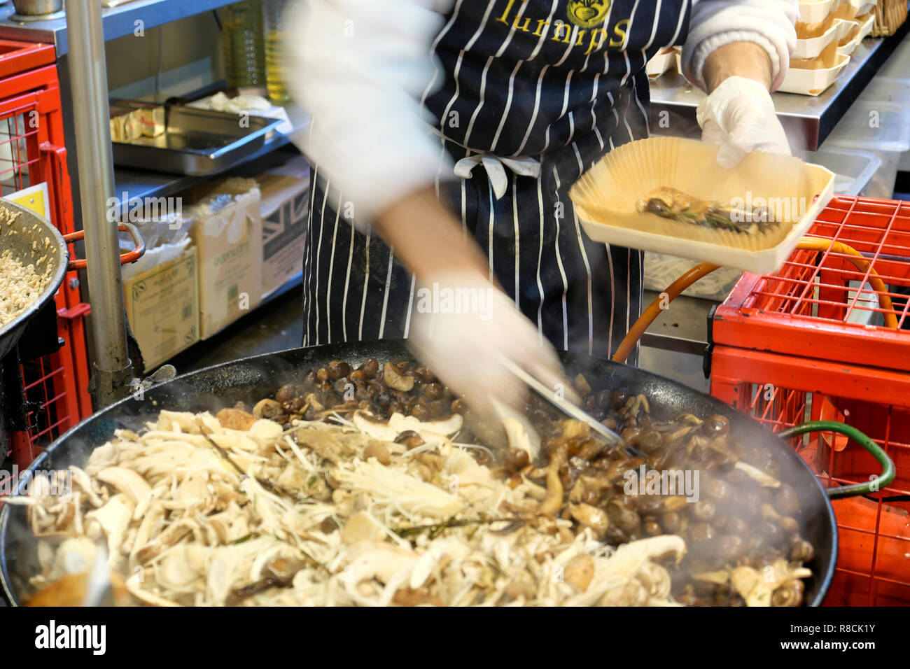 An Italian chef with an apron and gloves cooking hot wild mushroom