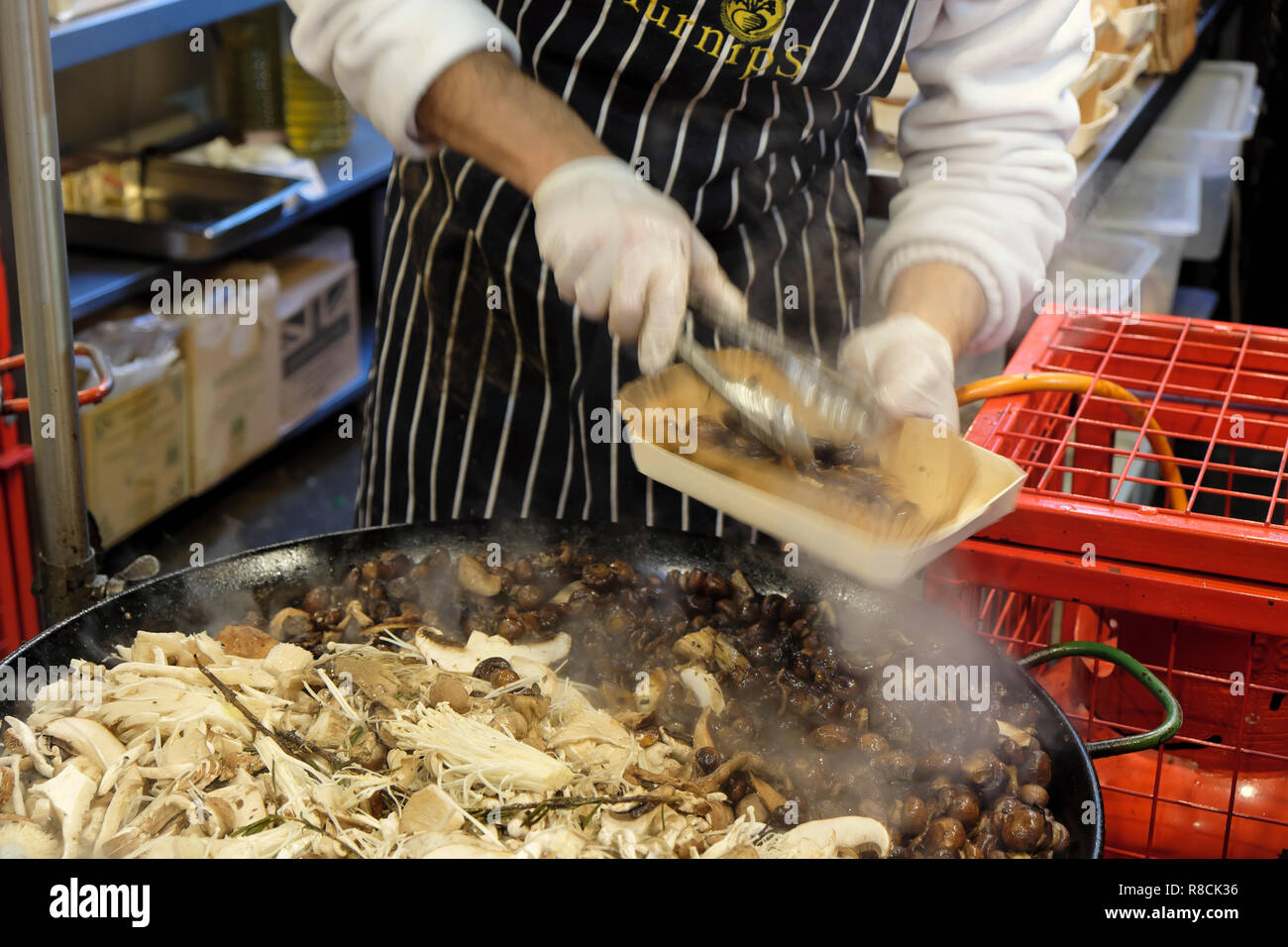 An Italian chef with an apron and gloves cooking hot wild mushroom