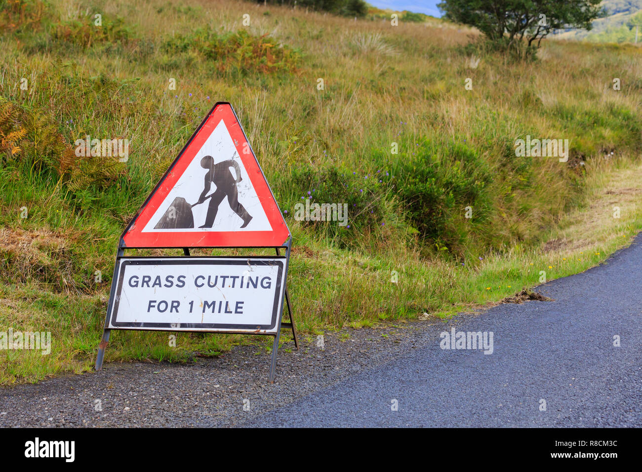 UK Triangle road sign warning of grass cutting for one mile Stock Photo
