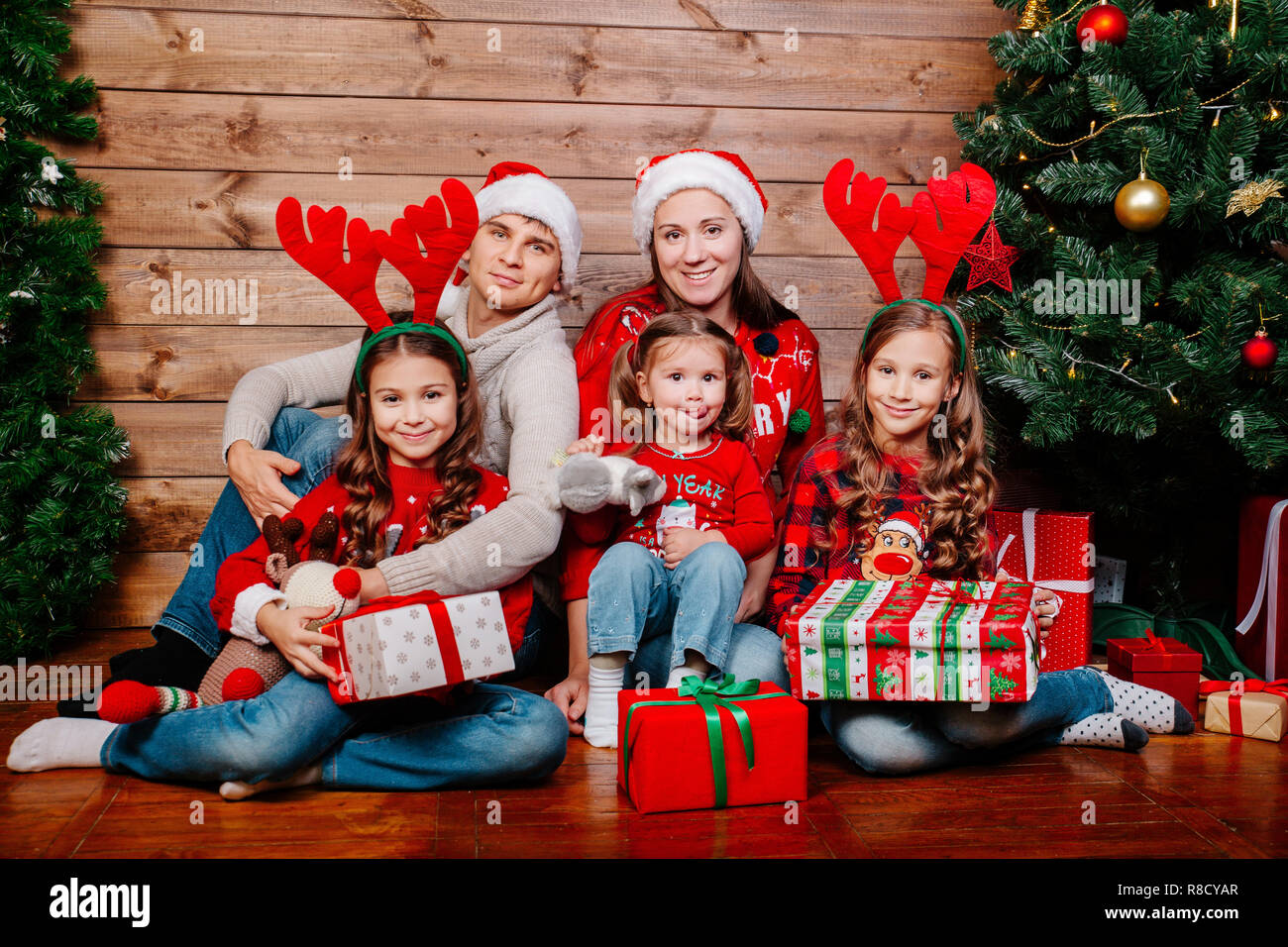Big smiling family in santa hats with many gift boxes sittting near Christmas tree at home. Merry Christmas and Happy Holidays Stock Photo