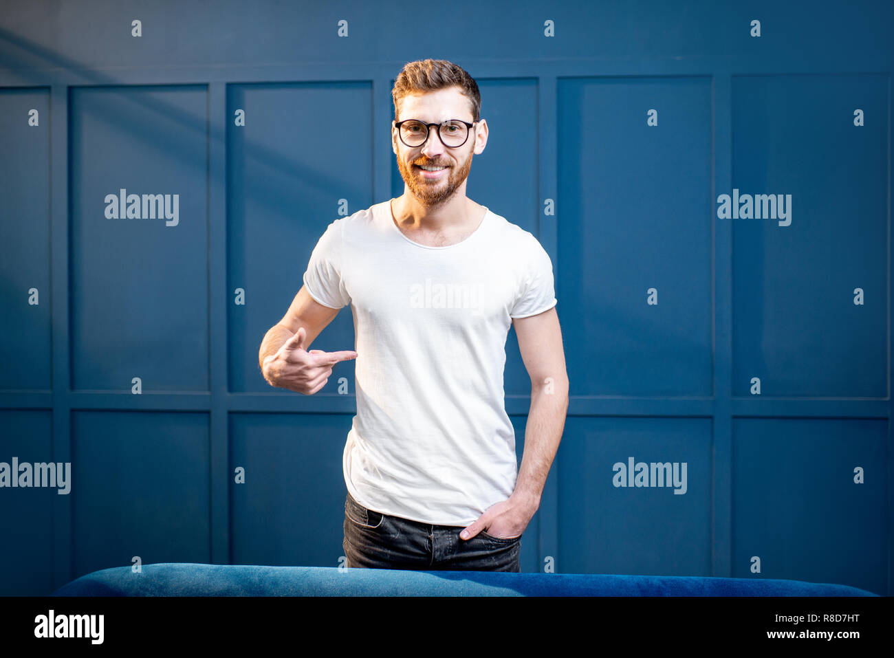 Portrait of a handsome man in white t-shirt with blank space to copy paste standing on the blue wall background Stock Photo