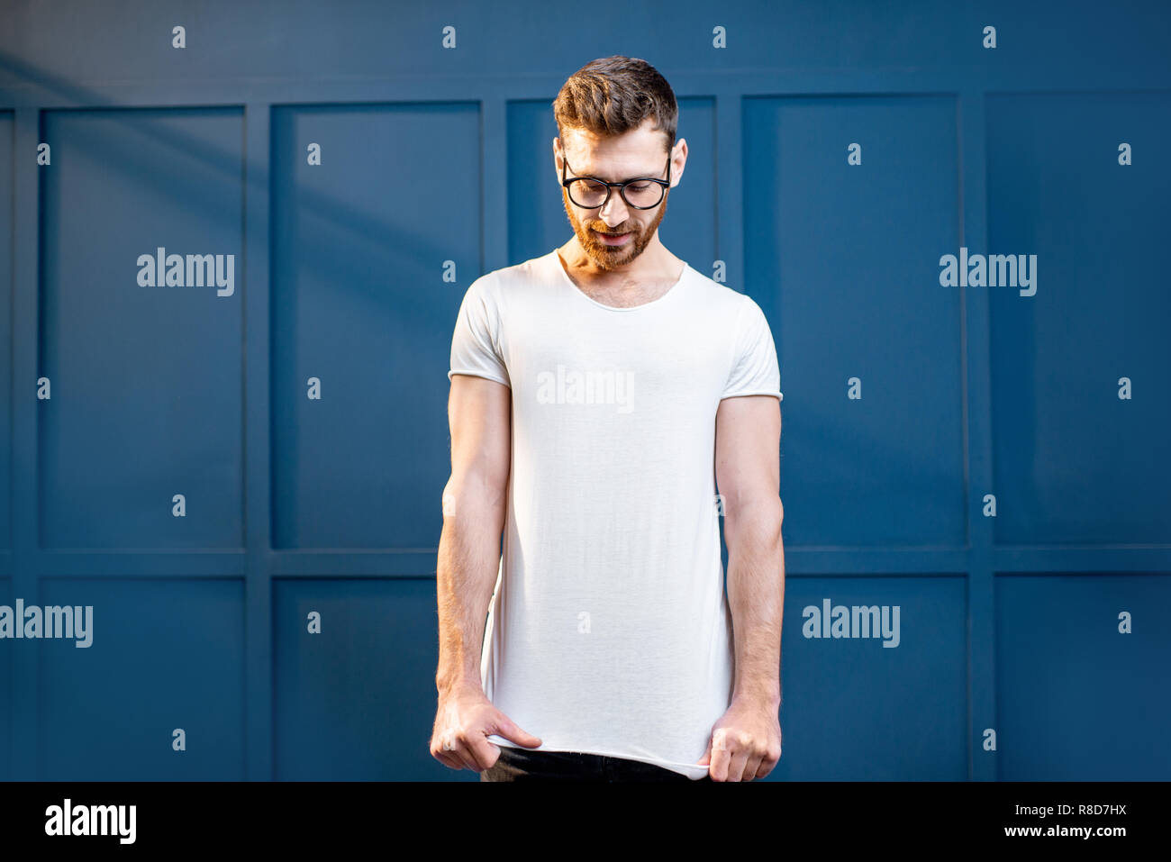 Portrait of a handsome man in white t-shirt with blank space to copy paste standing on the blue wall background Stock Photo