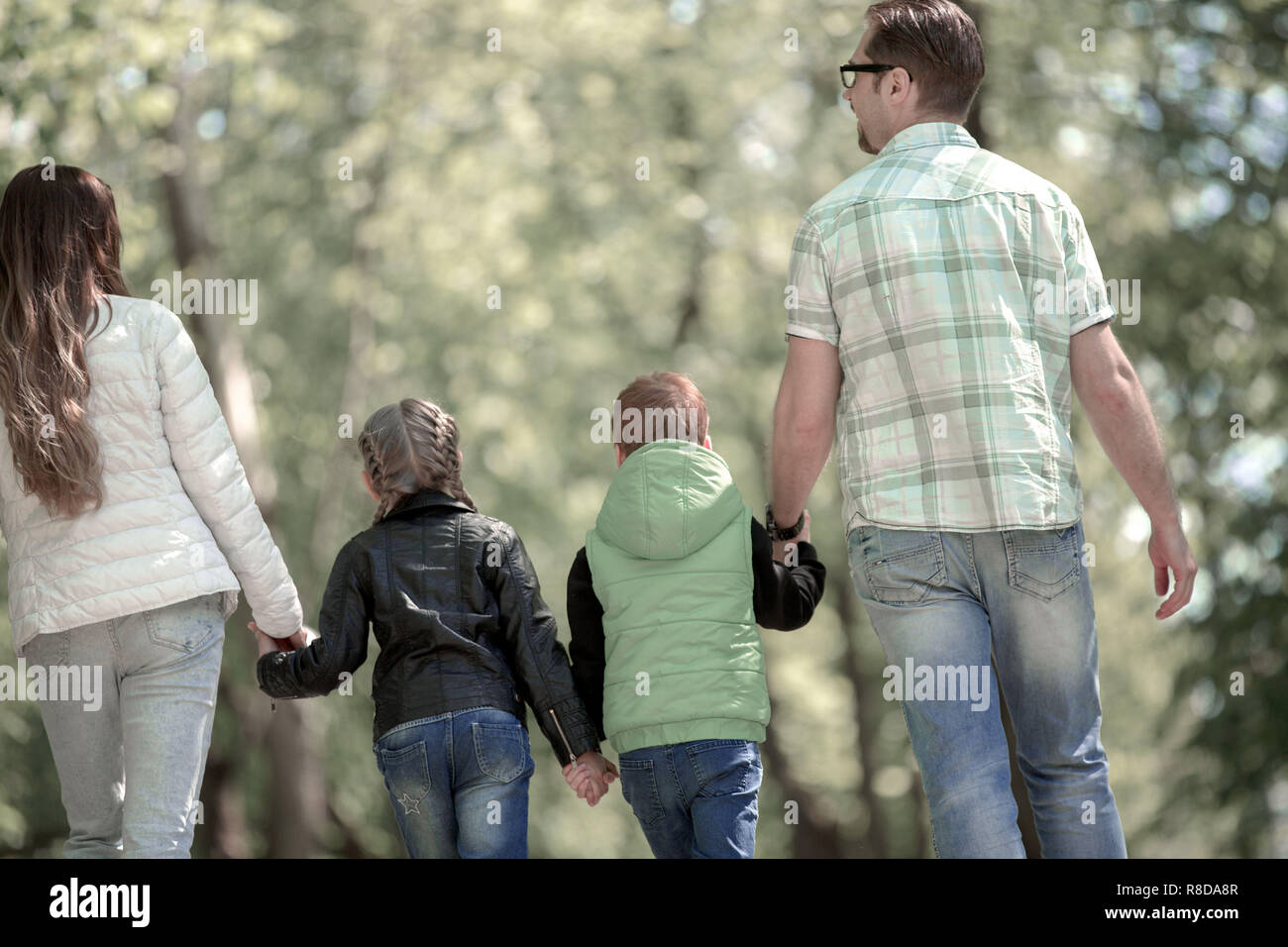rear view. family with two children walking hand in hand in the Park ...