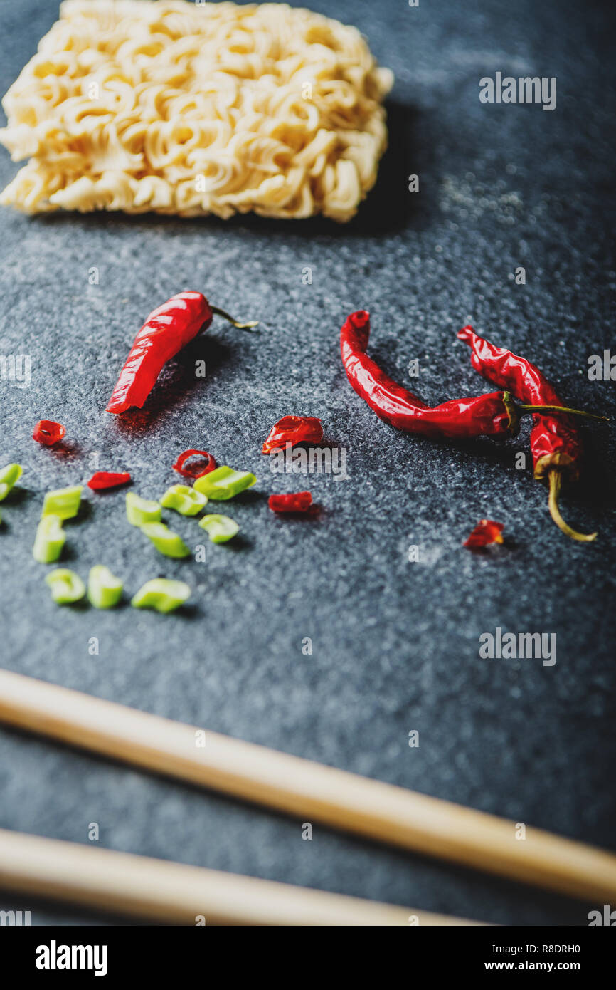 Asian instant noodles with and red chili peppers and green onion and chopsticks on black stone table Stock Photo