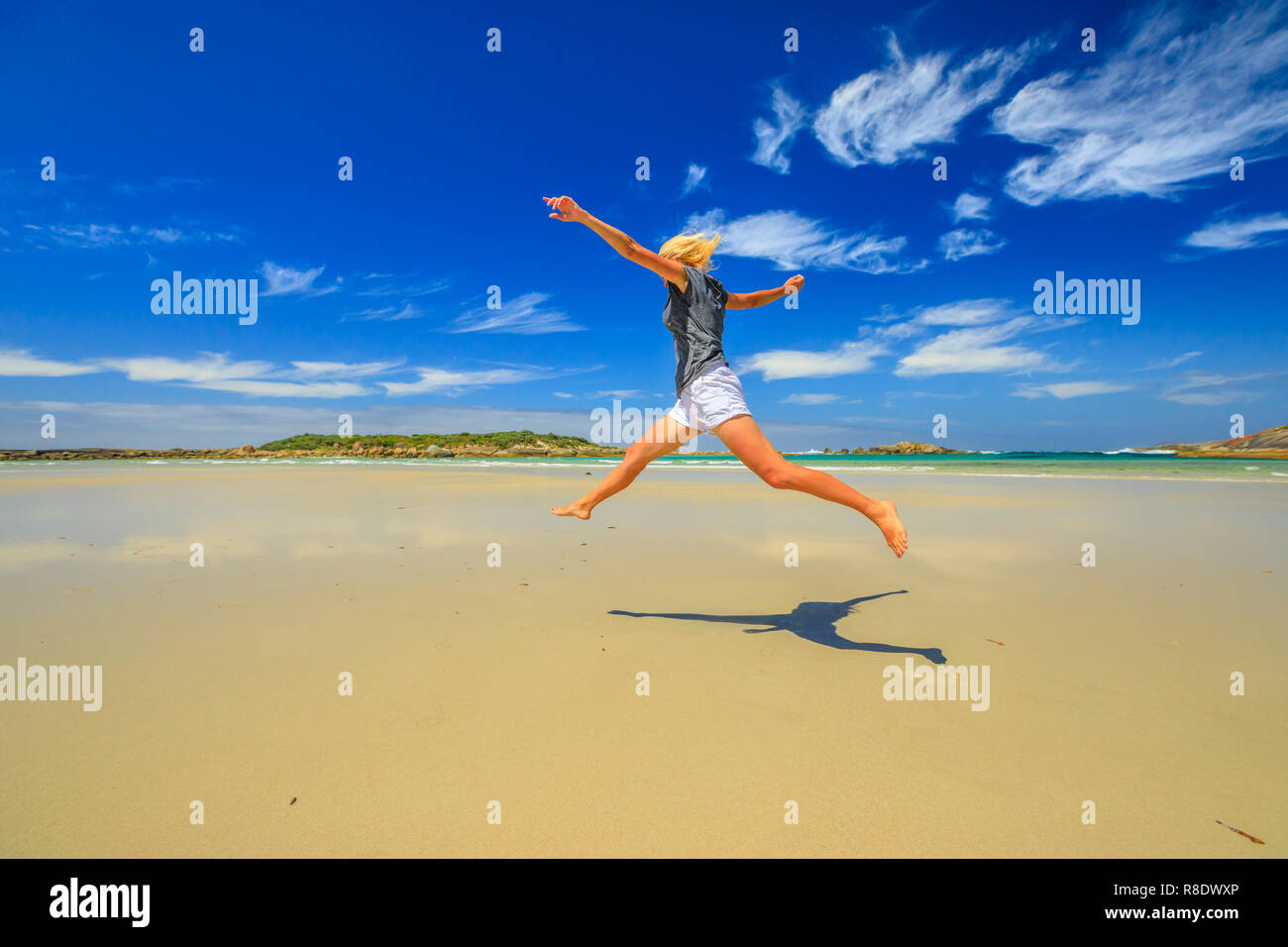 Joyful happy woman jumping on seashore of Madfish Bay in William Bay  National Park, Denmark region, Western Australia. Carefree girl jump. Beach summer  vacation in Australia. Copy space, blue sky Stock Photo -